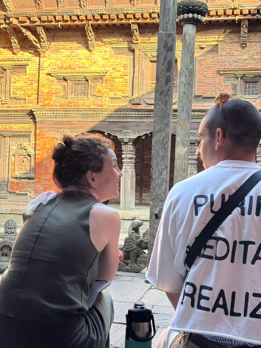 Mila and Lorenzo looking at each other while sitting near traditional architecture, showcasing their deep connection during their trip to Nepal.