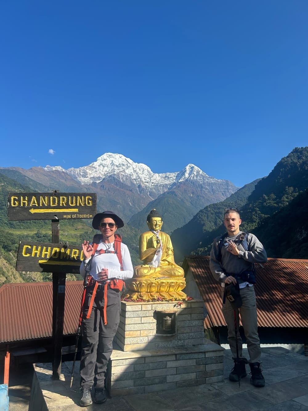 Mila e Lorenzo ao lado de uma estátua de Buda e placas de trilha durante seu trekking sustentável no Nepal. Mila e Lorenzo ao lado de uma estátua de Buda e placas de trilha durante seu trekking sustentável no Nepal.